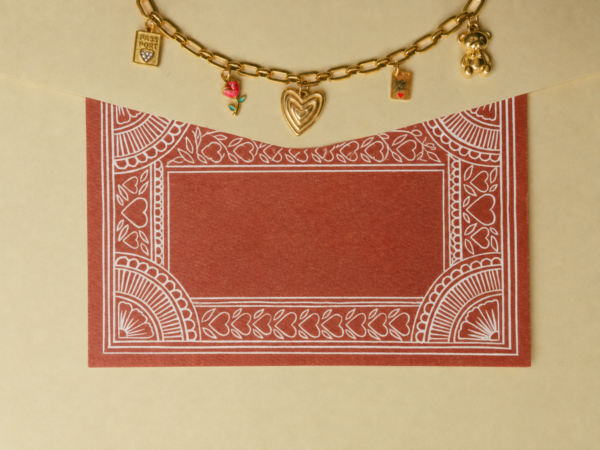 A square red card with a white ornate border pattern, displayed on a beige background with a gold chain necklace draped across the top.