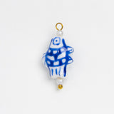 A small decorative bead or charm with a white base, blue hand-drawn style fish pattern, and gold-tone loop and bead accents, shown on a plain white background.
