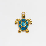 A small turtle-shaped jewelry charm with a gold-tone metal outline and a glittery blue shell, shown on a plain light gray background.